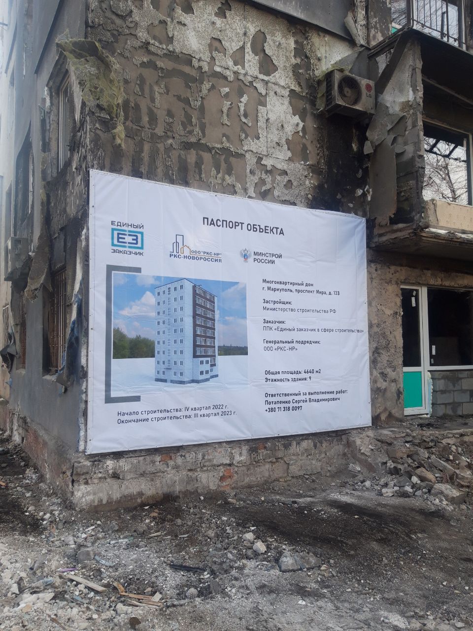 An official project-information sign ('ПАСПОРТ ОБЪЕКТА') mounted on the still-standing, fire-scarred facade of Lenina Avenue 133, listing builder, contractor, floor area, and a construction timeframe under the heading 'СТРОИТЕЛЬСТВО' (construction) — photographed 9 December 2022
