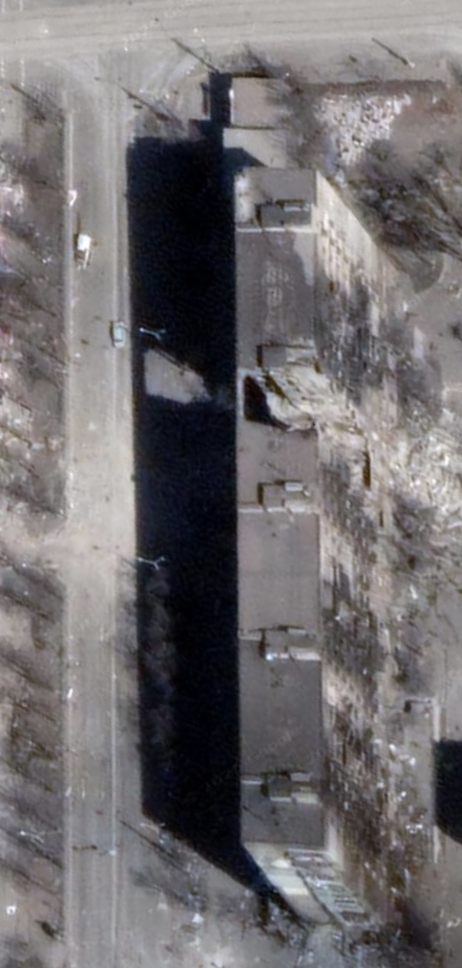 Satellite view, March 2022: the same building with one entrance section collapsed into a dark gap, snow on the ground.