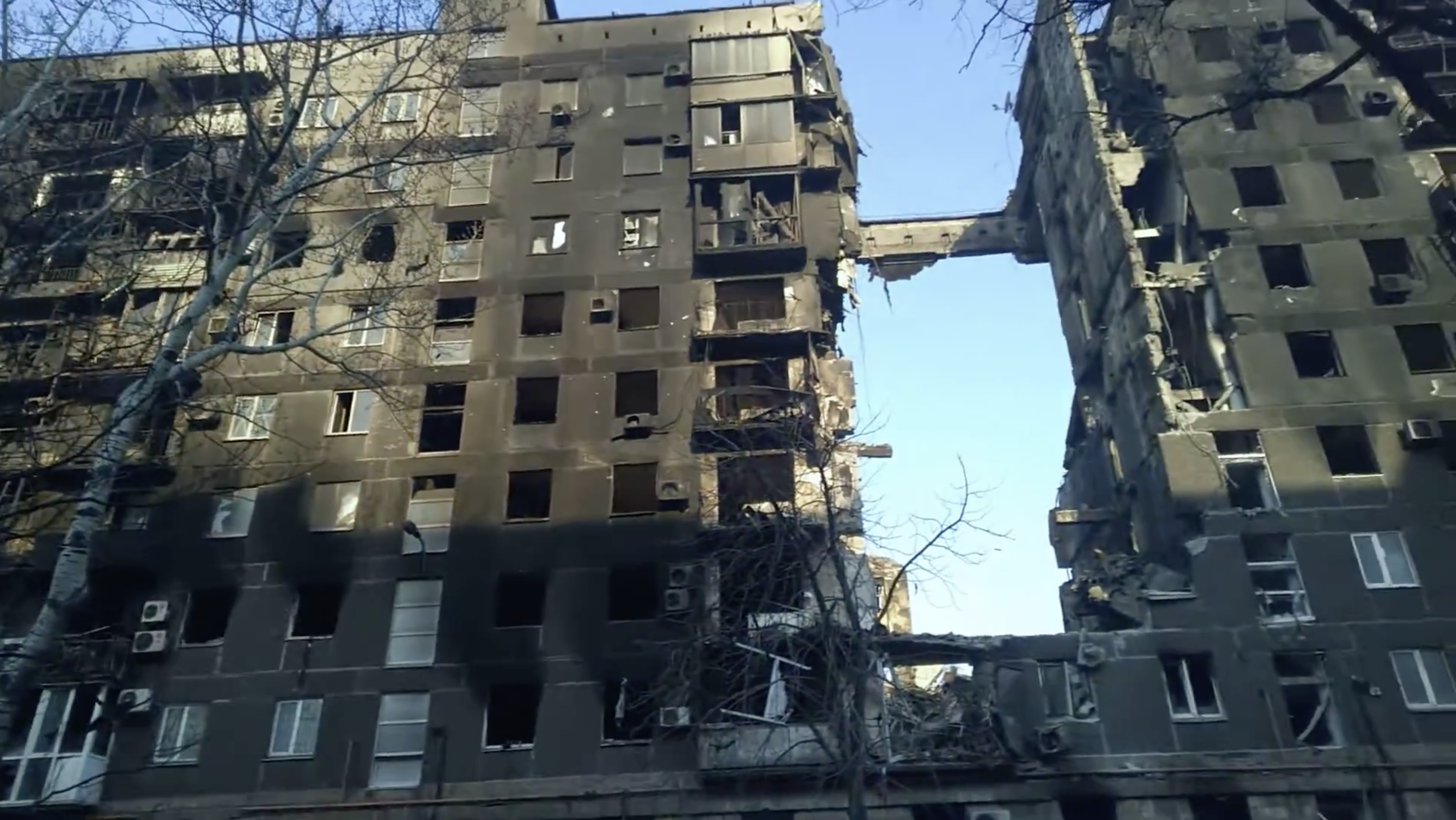 Closer street-level photograph, March 2022: fire-scorched facade either side of the collapsed entrance section, blown-out windows, balconies stripped to bare concrete.