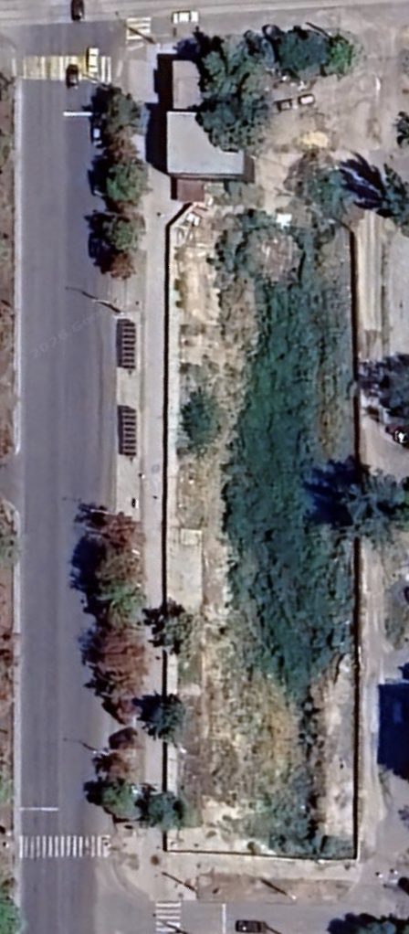 Satellite view, August 2024: the building demolished, the rectangular lot cleared to bare ground, the street trees still standing.